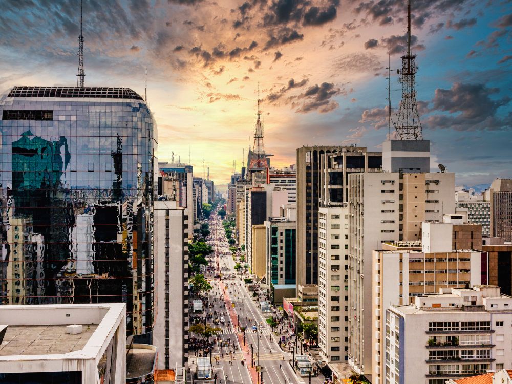 Vista da Avenida Paulista em São Paulo, com prédios modernos, antenas e movimento urbano ao pôr do sol