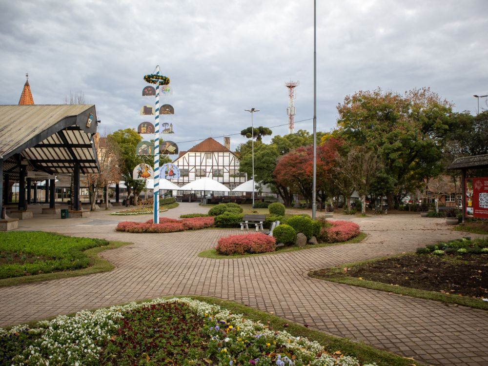 Praça arborizada em Joinville com jardim florido, arquitetura enxaimel ao fundo e espaço urbano organizado, representando ponto turístico tradicional da cidade.